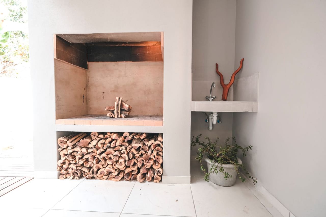 Built-in outdoor braai with stacked firewood storage and a corner utility sink