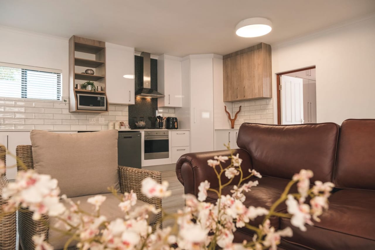 Open-plan kitchen with white cabinetry and stainless appliances beside a leather sofa and wicker chair