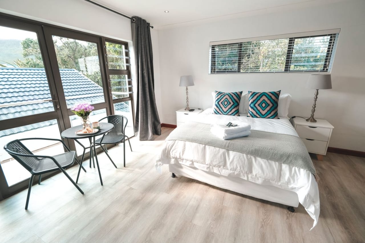 Bright studio bedroom with a white-linen double bed, bedside lamps and a window seating table